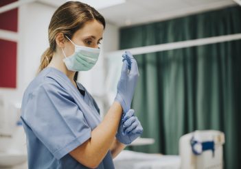 Female nurse with a mask putting on gloves